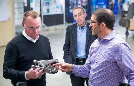 GM Director of Additive Manufacturing and Generative Design Kevin Quinn (right) shows Amend 3-D printed, proof-of-concept seat bracket.